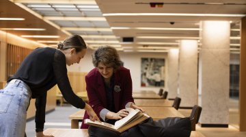 Two people bending over a desk and looking at a book.